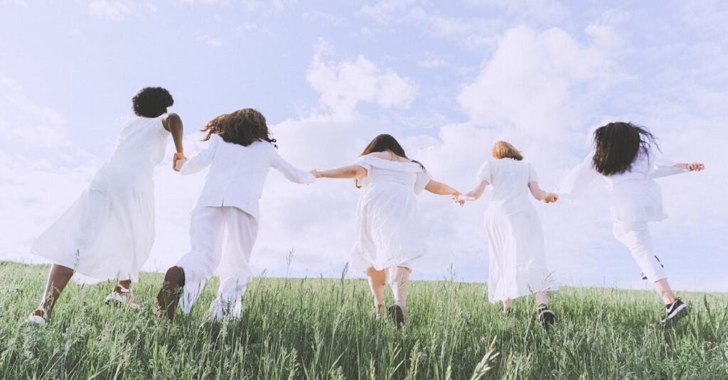 Five women joyfully running in a field under a clear sky, symbolizing freedom and happiness.